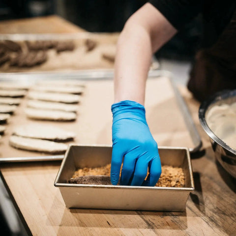Person wearing Blue Nitrile Gloves 3 Mil Textured Large Latex Free Powder Free Box Of 100, preparing food on a wooden surface.