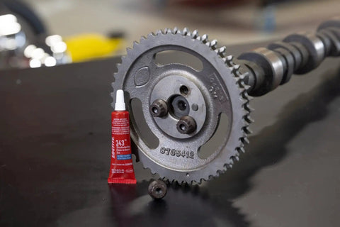 Blue 243 Oil-Resistant Threadlocker for Automotive Applications, 6 ml Tube next to metal gear and camshaft