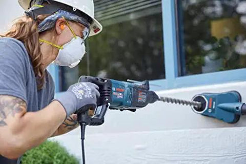 Person using Bosch Bulldog Extreme 1 Inch SDS Plus Rotary Hammer, drilling into concrete wall on site, showcasing 8 Amp motor power.