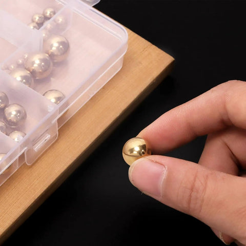 Close-up of hand holding a brass ball from Precision Brass Bearing Balls Set 120-Piece Assortment 3/32 To 1/2 Inch Sizes with storage box.