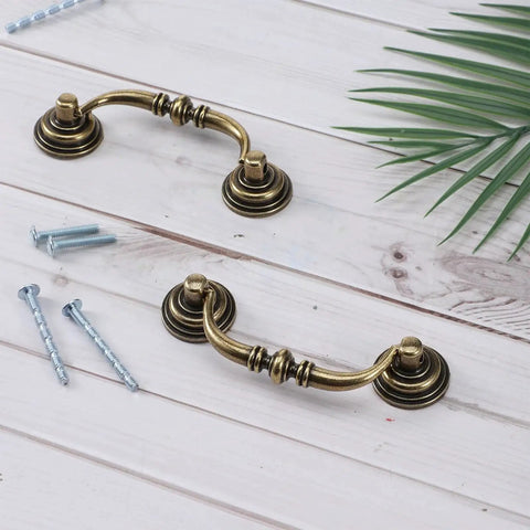 Two Bronze Vintage Drop Bail Drawer Pulls With 3.5 Inch Center Spacing And 4.5 Inch Total Length shown with screws on wood surface