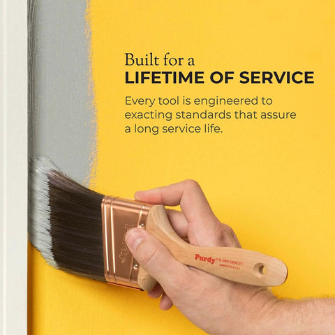 Hand holding a Purdy paintbrush applying gray paint on yellow wall, emphasizing durability and long service life.