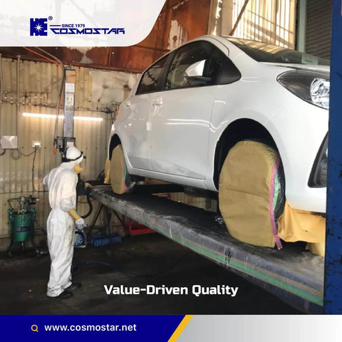 Car in workshop on lift being painted with protective covers on wheels and worker in protective suit and mask