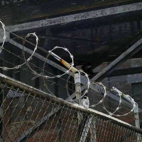 Barbed wire on chain link fence with industrial background, featuring 5" Pipe Track Wheel Galvanized, 1 7/8" Round Post for gate frame.
