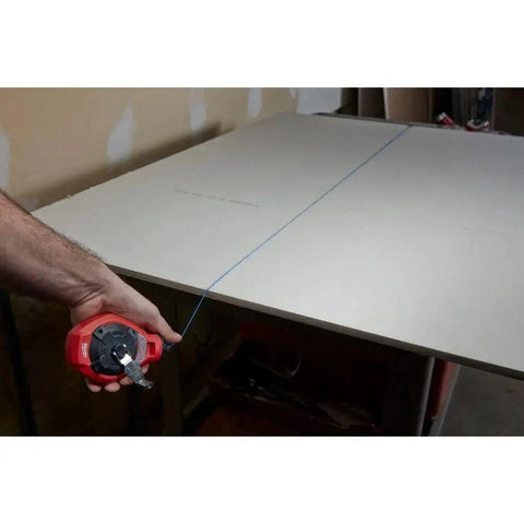 Milwaukee Chalk Line Reel Set F in use, showing 100 ft blue line marking a board for precise layout on construction project.