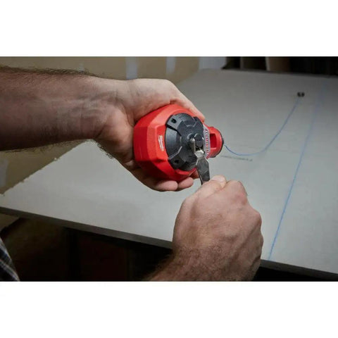 Person holding Milwaukee Chalk Line Reel Set F with 100 ft blue line, drawing layout mark on grey surface.