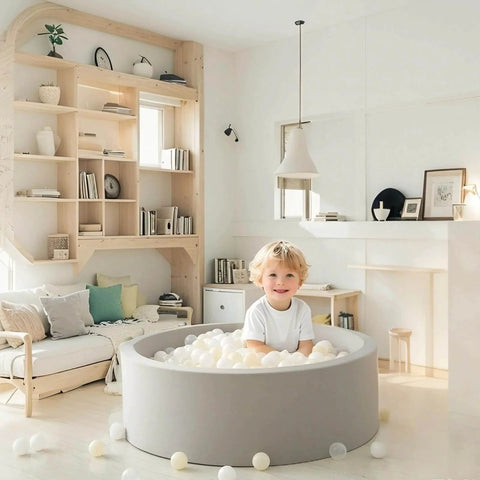 Child playing in a grey indoor ball pit with Ball Pit Balls Plastic Playballs for Baby Toddlers Kids Boys Girls Playhouse Decor Play Pool Fun Phthalate-Free BPA-Free Bath Toy White Beige Transparent,100 Balls in a cozy living room.
