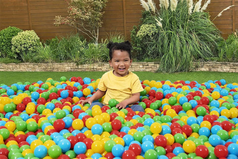 Child playing in Play Balls 100ct set, colorful plastic balls for indoor play, ball pits, and bouncers, in a garden setting