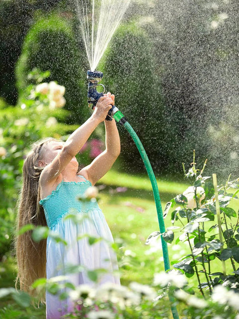 Child watering garden with hose, using sprinkler nozzle.