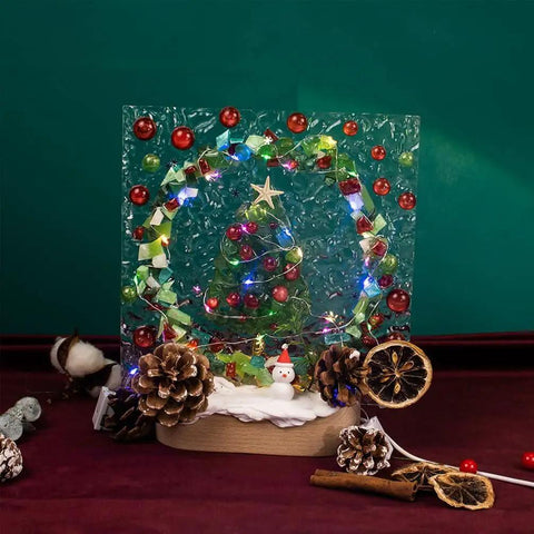 Christmas-themed decoration with pine cones, lights, and a snowman on a rustic base, set against a festive green background.