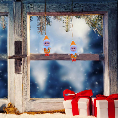 Two elf ornaments hanging by a snowy window with pine branches, next to a stack of gift boxes wrapped in red bows.