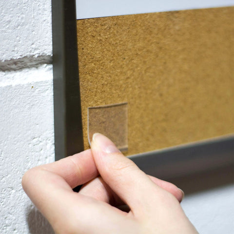 Person applying Tough And Clear Double Sided Tape Squares For Mounting, 24 Pre-Cut 1-Inch Squares to wall for indoor use
