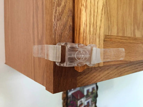 Clear self adhesive safety latches on wooden cabinet corner for childproofing, 9-inch length, no tools required, with four flaps.