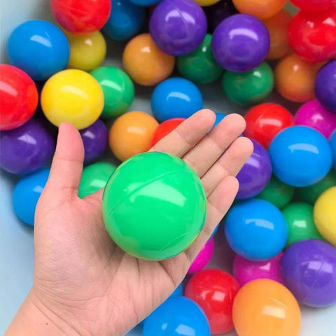 Hand holding a green ball from Colorful Ball Pit Balls 100pcs for Kids, BPA & Phthalate Free, Crush Proof, Non-Toxic, in background with mix colors
