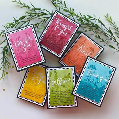 Colorful handmade greeting cards with floral designs and gratitude messages arranged on a leafy background.