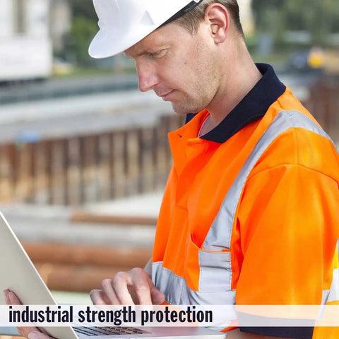 Construction worker in orange safety vest using a laptop at a construction site with blurred background.