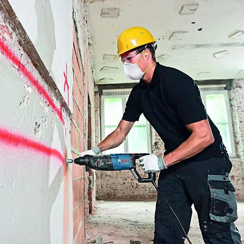 Worker using a powerful 8.5 Amp corded SDS-Plus rotary hammer with 2.4 ft-lbs impact energy for fast drilling in a concrete wall.