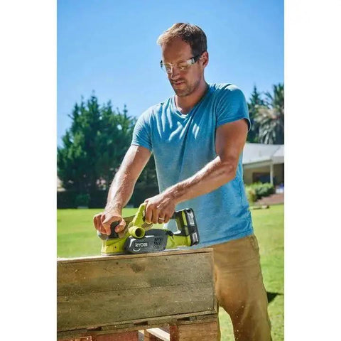 Man using Cordless 18V Planer with a compact 3-1/4 inch width and included dust bag on a wooden plank outside in a garden.