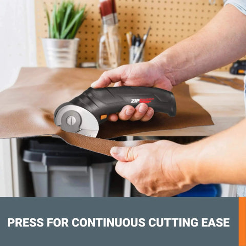 Person using ZipSnip Cordless Electric Scissors 4V Box Cutter for Fabric, cutting brown fabric in workshop with tools in background.