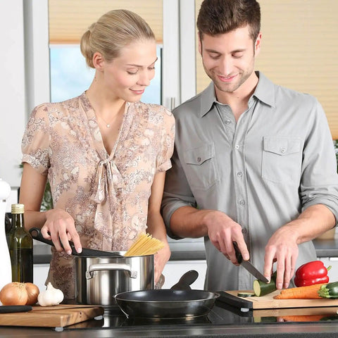 Two people cooking in a kitchen, using cutting boards and various utensils, preparing vegetables and pasta in a casual setting.