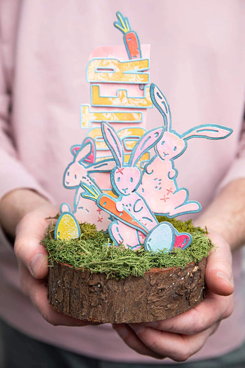 Decorative Easter centerpiece with rabbits, carrots, and Alphanumeric Emporium Thinlits Die Set 41PK crafted letters on wood slice.