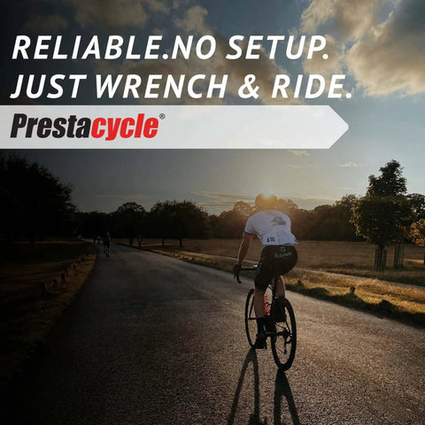 Cyclist riding a bike on a scenic road at sunset with 'Reliable. No Setup. Just Wrench & Ride' text and Prestacycle logo.