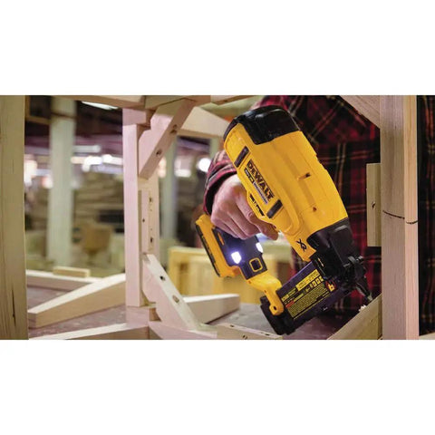 Person using DEWALT 20V MAX cordless 18GA brad nailer kit with LED work light on wooden frame for precise nail placement