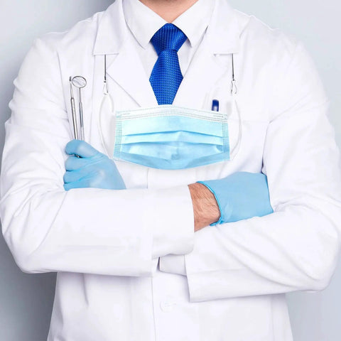 Doctor in white coat with blue tie and gloves, holding dental tools, wearing a mask and stethoscope.