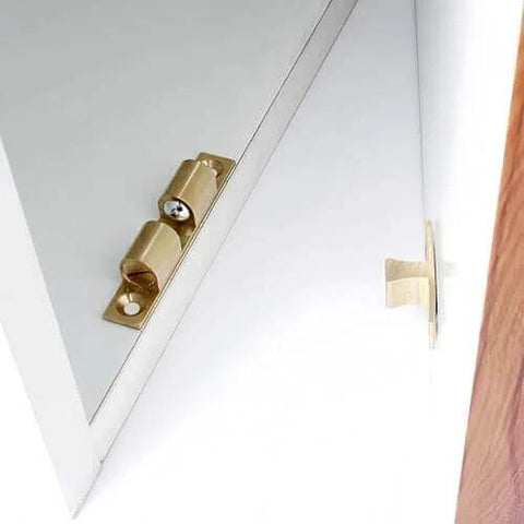 Brass spring detent latch on white cabinet door, angled view for precise positioning, indexing, locking in mechanical equipment.