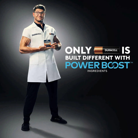 Person in a lab coat holding Alkaline AAA Batteries 24 Count Pack With Power Boost For Long Lasting Power, standing against a dark background.