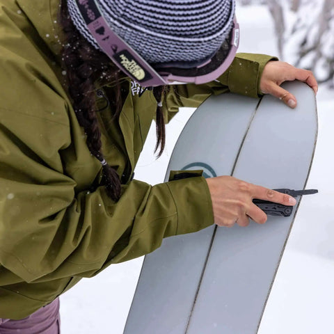 Person using Suspension-NXT 15-In-1 EDC Multi Tool With Pocket Knife and Pliers on snowboard edge in snowy setting