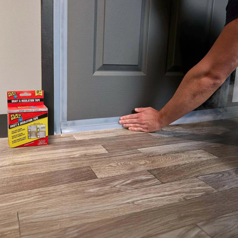 Applying Flex Seal Draft and Insulation Sealing Tape, 2 in x 16 ft, clear rubberized strip to door; pack visible beside hardwood floor