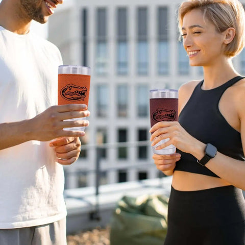 Two people holding Florida Gators Engraved 20 Oz Grip Tumblers with Vacuum Insulated Double Wall Stainless Steel Travel Mugs outdoors.