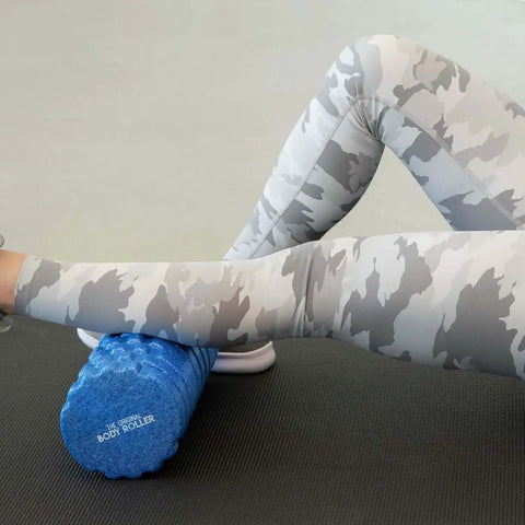 Person using a blue high density foam roller massager with 3D textured rollers for deep tissue back and leg muscle massage on yoga mat.
