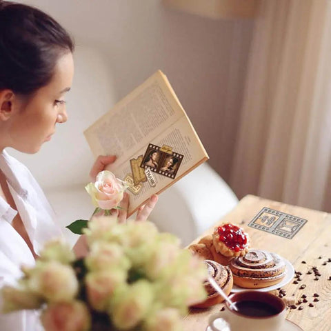 Woman reading a book with Awesome Versatile Die Cut Set For Card Making And Scrapbooking; floral decor and pastries on table.
