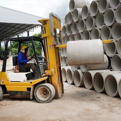 Forklift with 84 Inch Fork Extensions For Forklifts in use lifting concrete pipe at a construction site.
