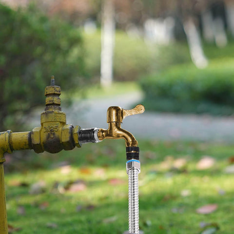 Outdoor water faucet with garden hose attached in a garden setting.