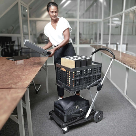 Person using Original German Made Collapsible Cart With Storage Crate Multiuse Folding Trolley For Shopping Hotels Catering Warehouse And Food Service Lightweight Aluminum Frame With Durable Polypropylene Cargo Box Black in office setting