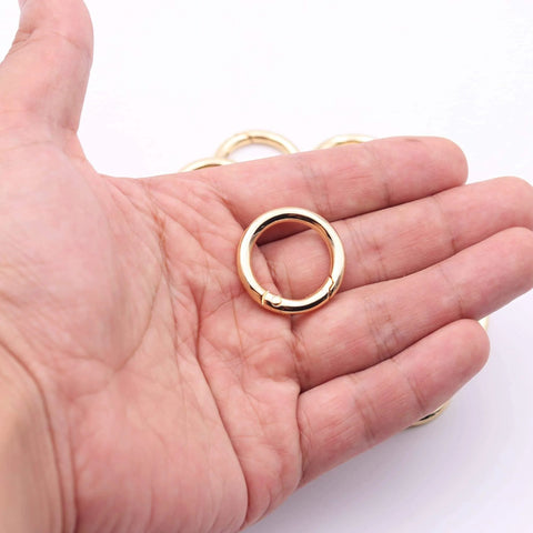 Hand holding a gold Three Quarter Inch durable zinc alloy carabiner from the Twenty Pack Trigger Spring Round Carabiner Clips Snap Hooks.