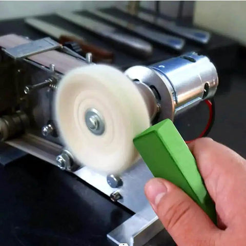 Hand holding green buffing compound bar for metal polishing against rotating buffing wheel on metal surface