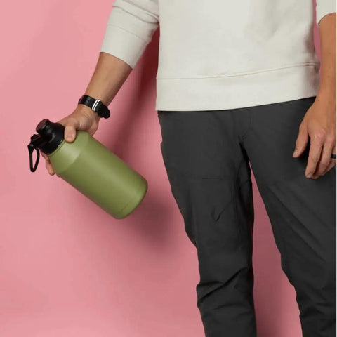 Person holding a green water bottle against a pink background, wearing a white sweatshirt and dark pants.