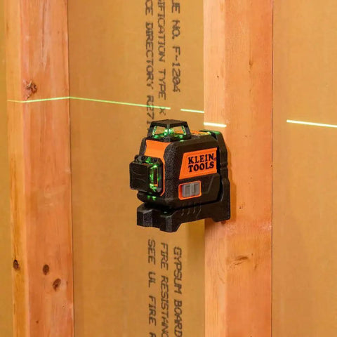 Compact self-leveling laser level with bright green cross lines and 360-degree planes on wood surface for construction alignment.