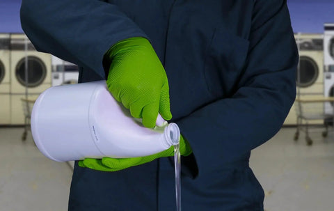 Person using Green Nitrile Latex Free Gloves 8 Mil Heavy Duty Raised Diamond Texture Box 100, pouring liquid detergent in laundry setting