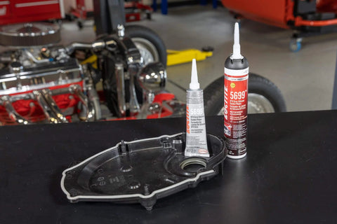 Two tubes of RTV Grey High Performance Silicone Gasket Maker For Oil Resistant Seals in a garage with auto parts