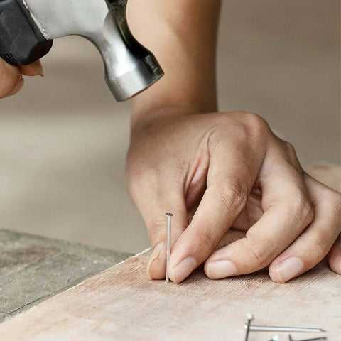 Person hammering a silver nail from 600 Piece Nail Assortment Kit Silver Nails In 4 Sizes For Hanging Pictures And Finishing Nails.