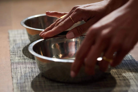 Hands holding stainless steel bowls on a textured mat