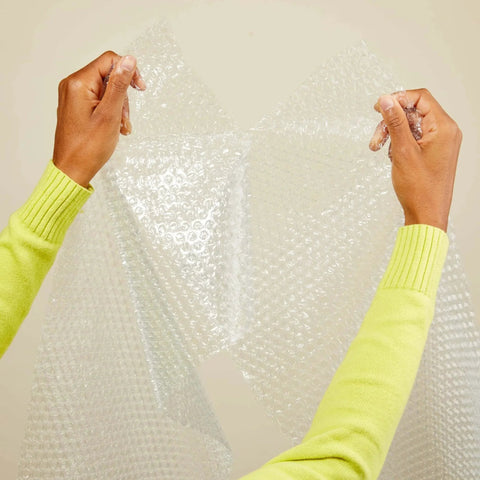 Hands tearing clear perforated bubble cushioning wrap for fragile items perforated 12 inch roll 175 ft clear with small three sixteenth inch bubbles.