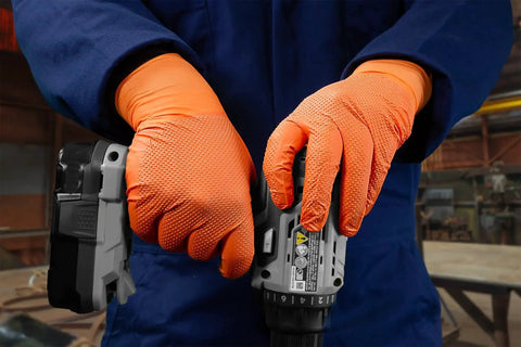 Person wearing Hi Vis Orange Nitrile Gloves Raised Diamond Texture 8 Mil using a power tool in workshop