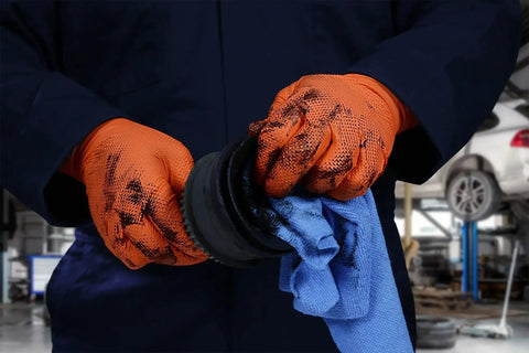 Worker wearing Hi Vis Orange Nitrile Gloves Raised Diamond Texture 8 Mil, holding tools in a mechanic shop