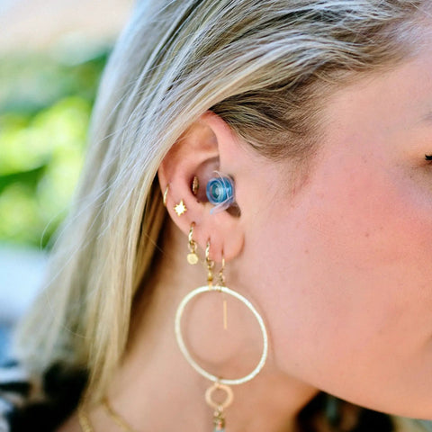 Close-up of a woman wearing high fidelity reusable earplugs with blue filters for concerts and live music offering superior noise reduction.